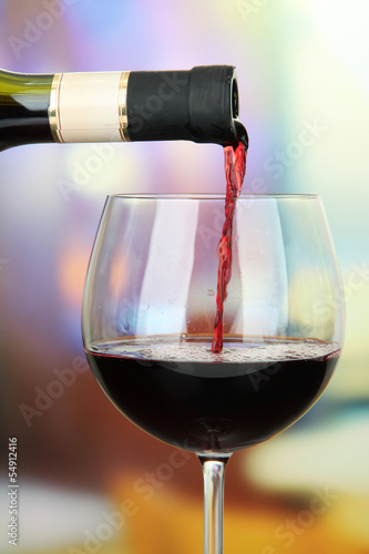 Red wine being poured into wine glass, on bright background