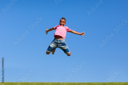 Outdoor portrait of a cute teenage black boy jumping over a blue