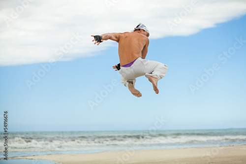 erwachsener sportlicher mann am strand springt karate
