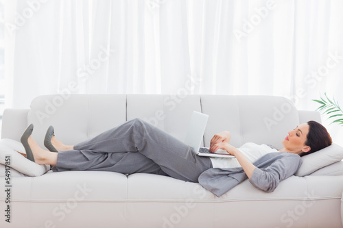 Businesswoman using her laptop lying on sofa