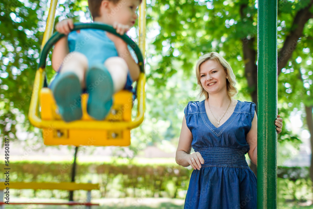 Obraz premium Young caucasian mother with swinging son at playground