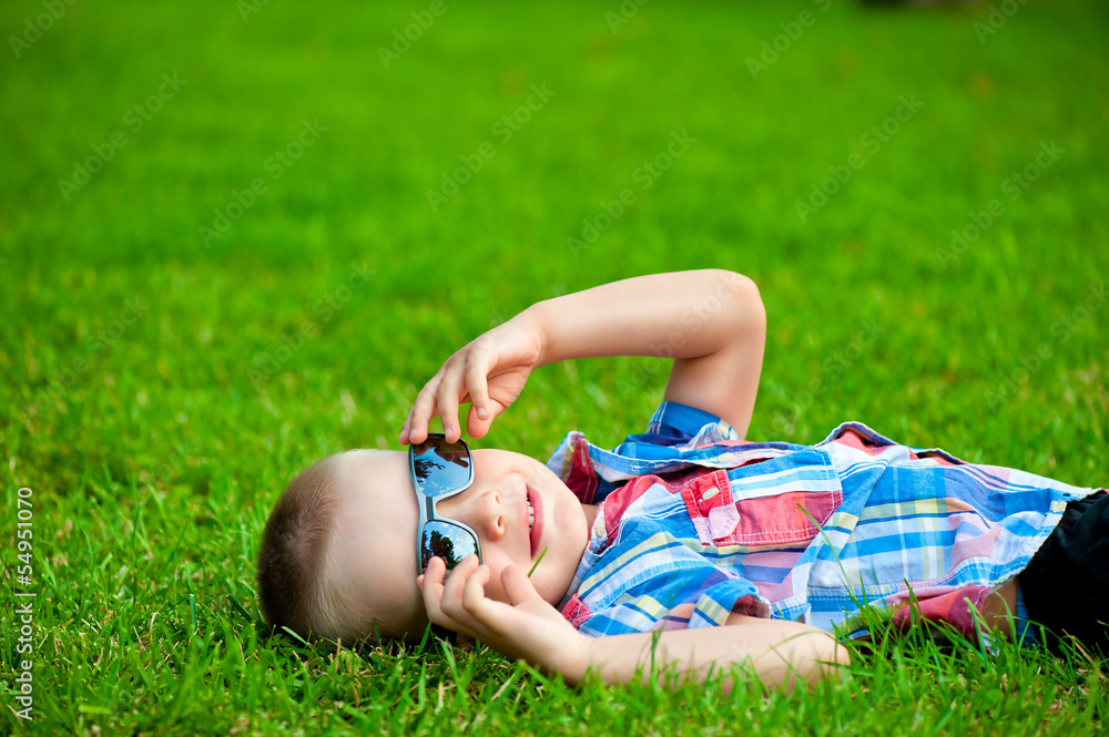 happy boy resting lying on green grass in sunglasses happy boy resting lying on green grass in sunglasses