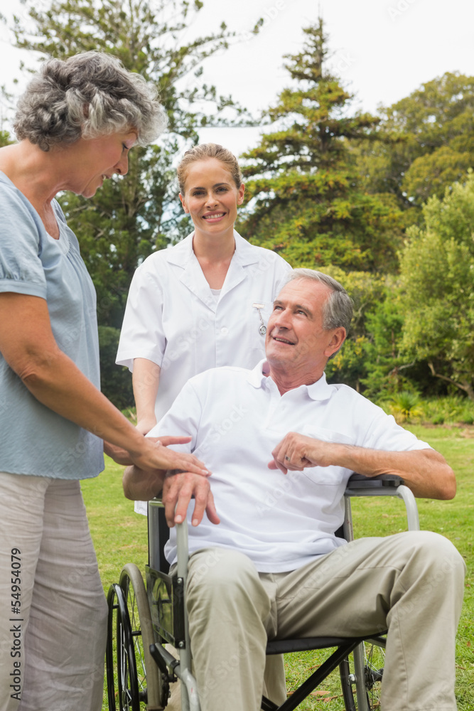 Happy man in a wheelchair talking with his nurse and wife Happy man in a wheelchair talking with his nurse and wife