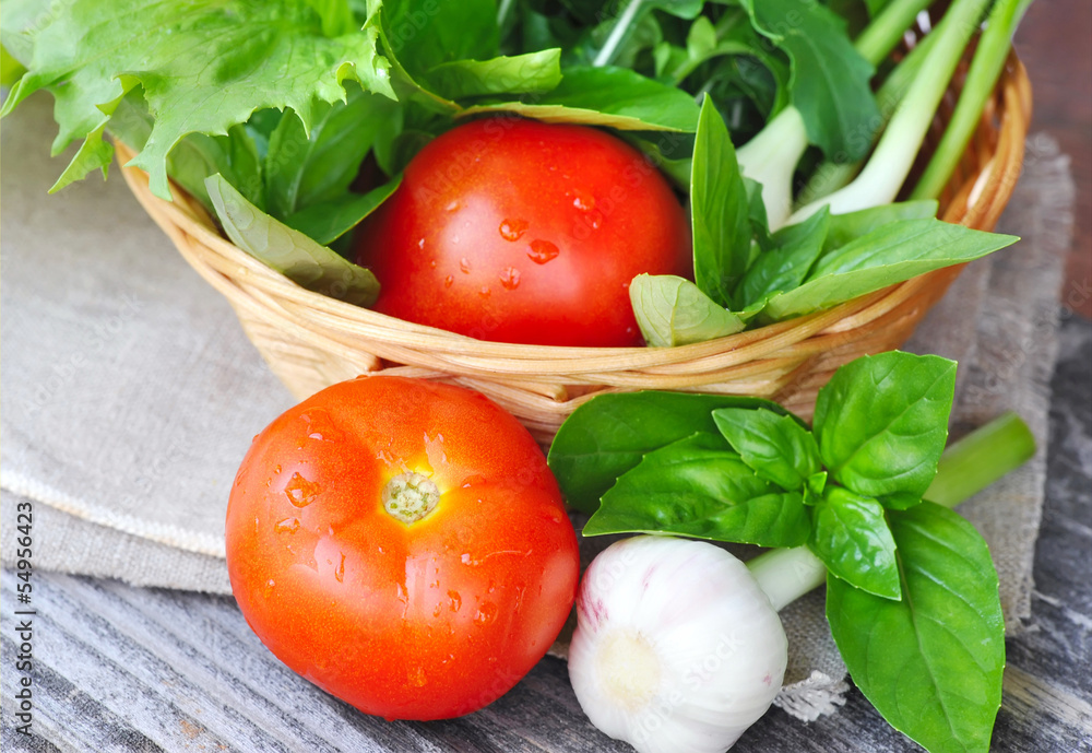 Fresh vegetables and greenery are in a basket on a wooden Fresh vegetables and greenery are in a basket on a wooden