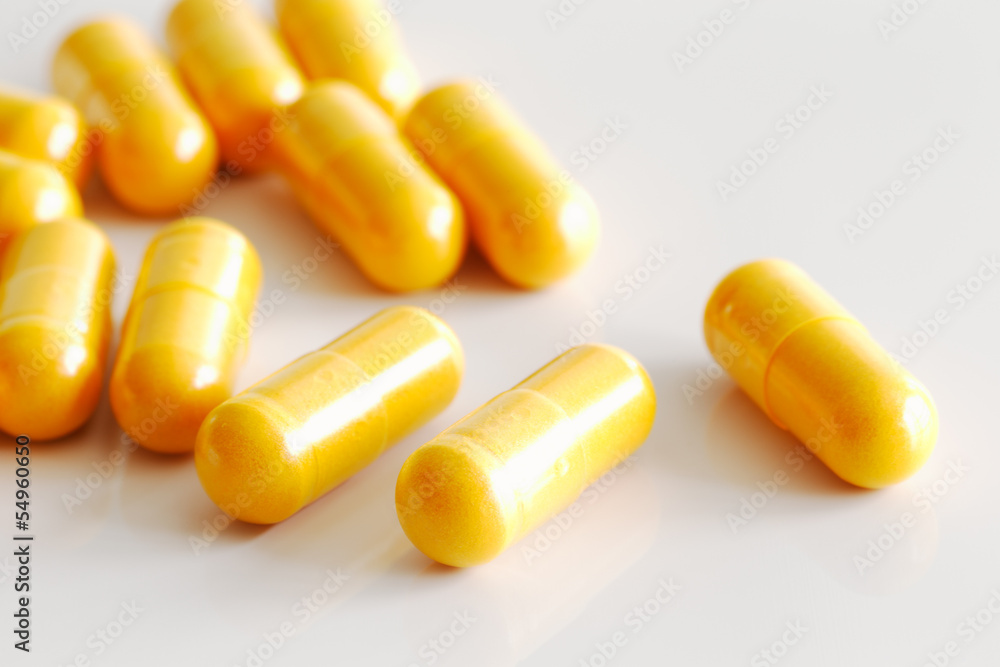 Handful of turmeric capsules on white reflective ceramic surface Handful of turmeric capsules on white reflective ceramic surface