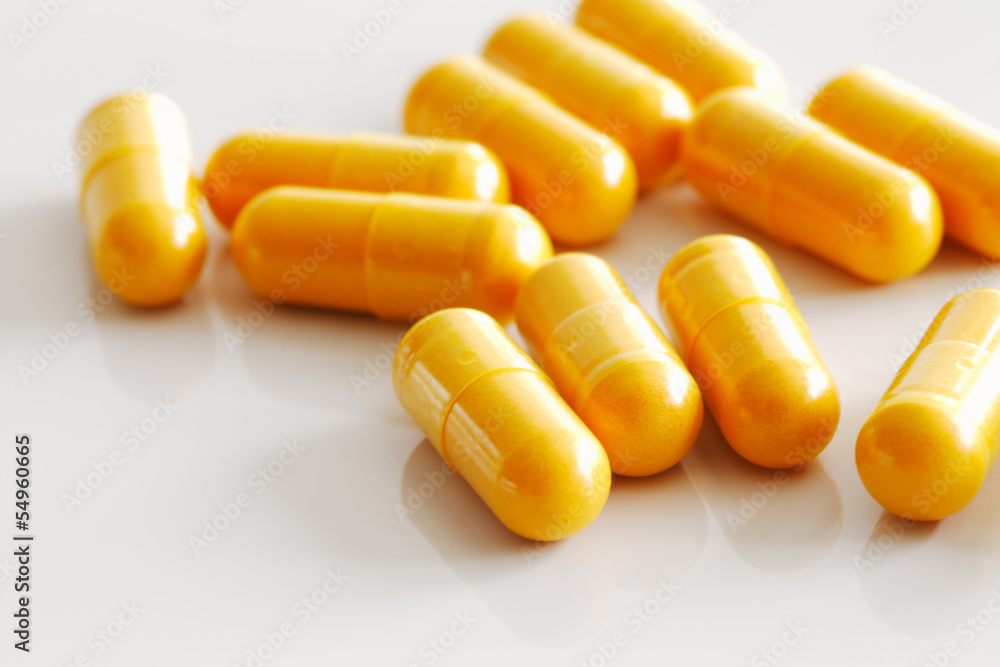 Handful of turmeric capsules on white reflective ceramic surface Handful of turmeric capsules on white reflective ceramic surface