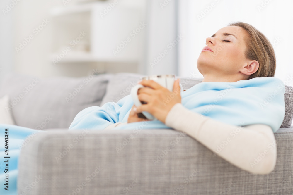 Ill woman with cup of hot beverage sitting on couch Ill woman with cup of hot beverage sitting on couch