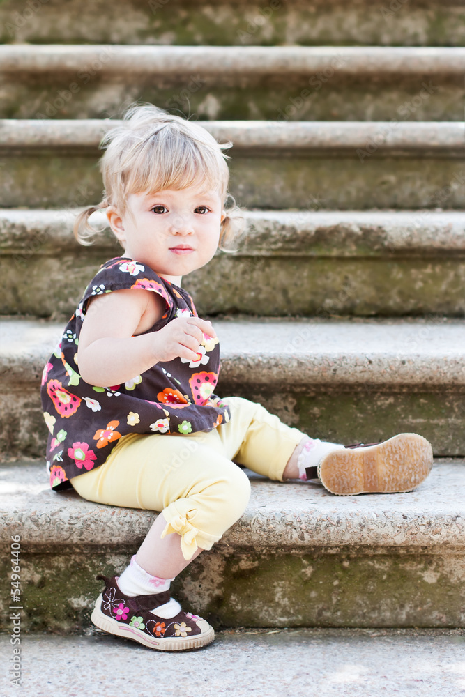 Fototapeta premium Little cute girl in sitting on the stairs with stone steps