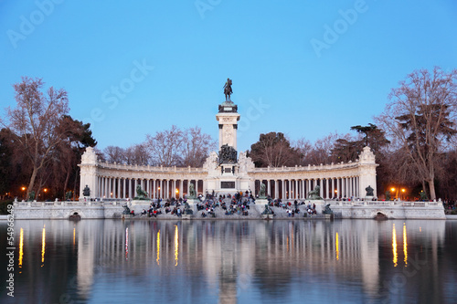 Tourists sit near monument to Alfonso XII at pond in Retiro Park