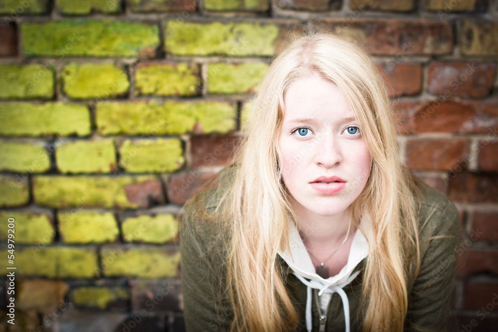 Blond girl with blue eyes in front of old brick wall Blond girl with blue eyes in front of old brick wall