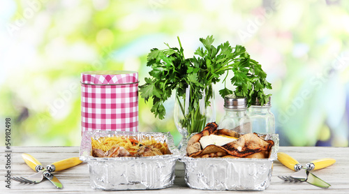 Food in boxes of foil on wooden table on nature background