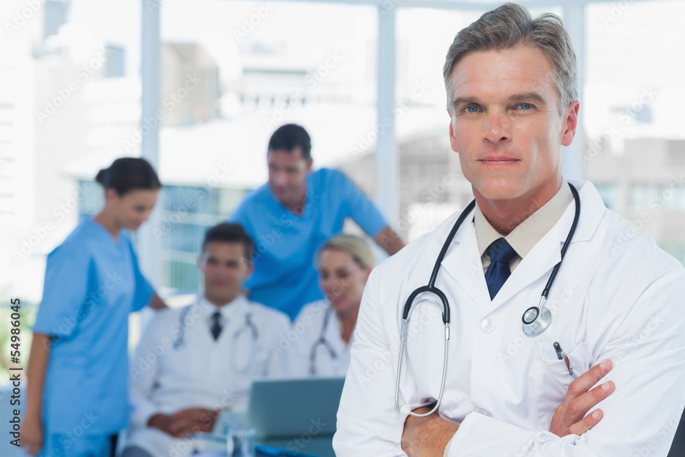 Experienced doctor posing with colleagues in background Experienced doctor posing with colleagues in background