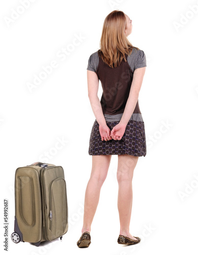 Back view of traveling blonde woman in dress with suitcase looki