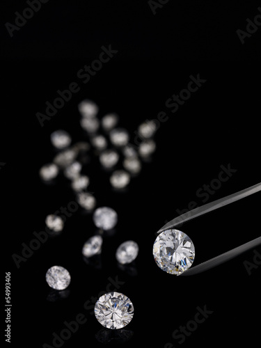 Tweezers and cut diamonds against black background photo