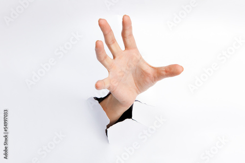 Female hand reaching through torn paper sheet