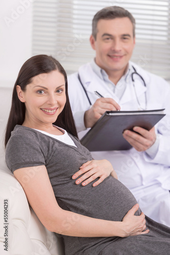 Medical exam. Confident mature doctor sitting near pregnant woma