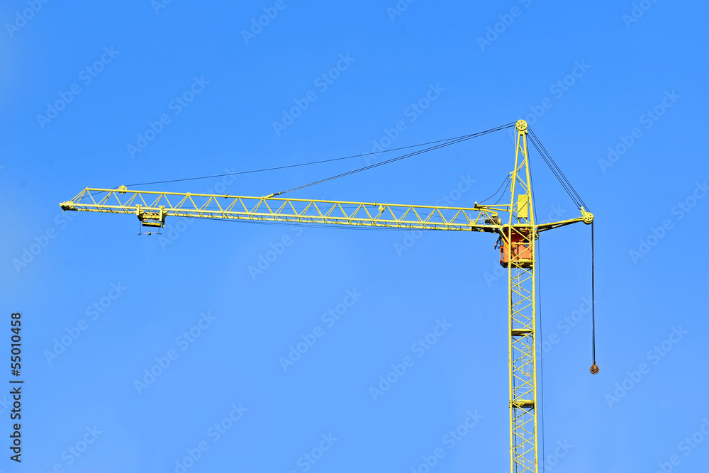 Yellow construction tower crane against blue sky Yellow construction tower crane against blue sky