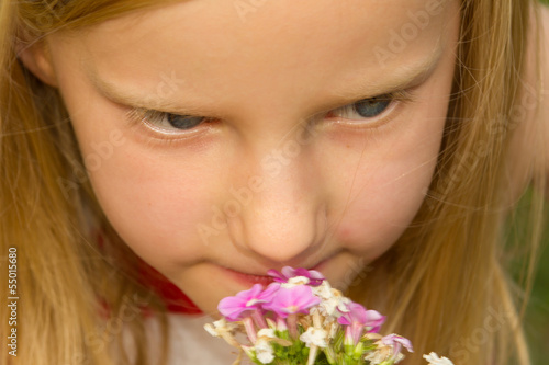 Adorable young schoolgirl smelling pink flower on a sunny day cl