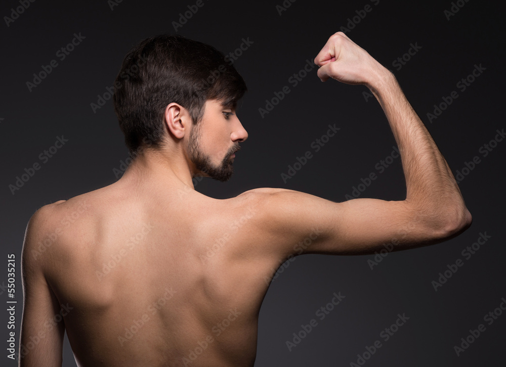 Strong young man. Rear view of shirtless man posing while isolat Strong young man. Rear view of shirtless man posing while isolat