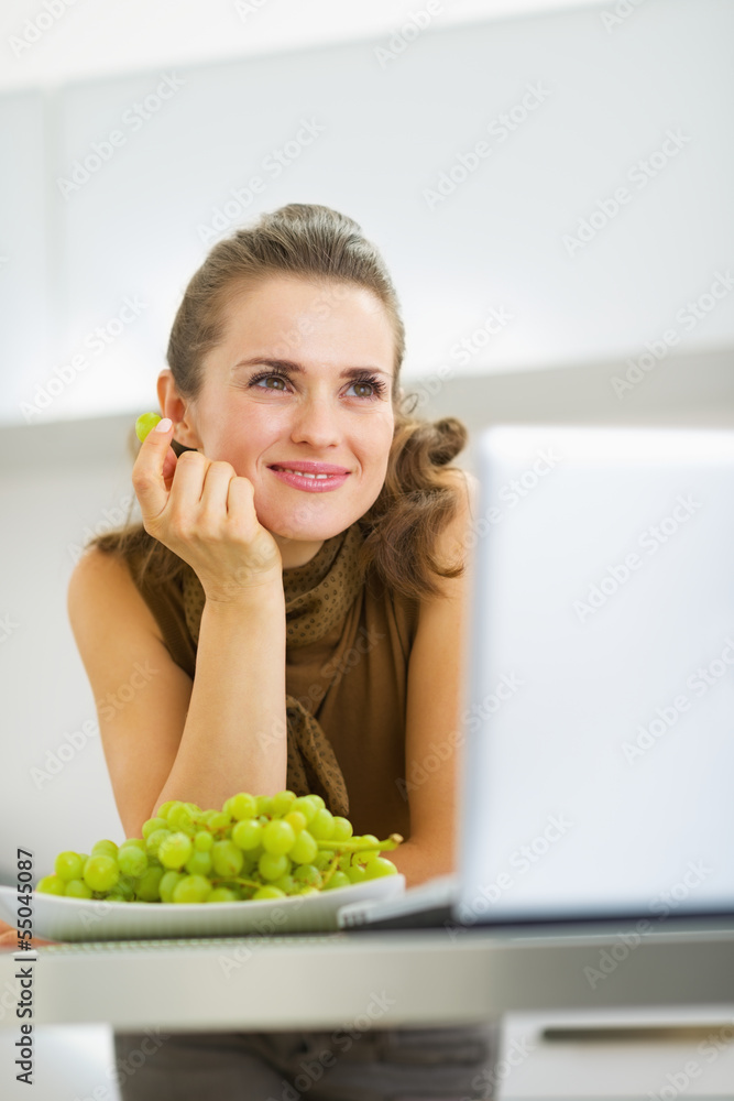 Dreaming young housewife eating grape in kitchen Dreaming young housewife eating grape in kitchen
