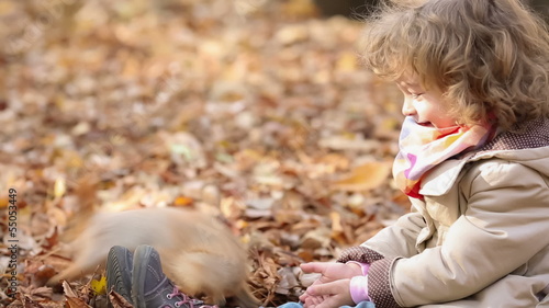 Happy child feeds a little squirrel in autumn park