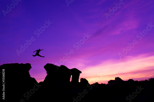 Silhouette man jumping between two stone