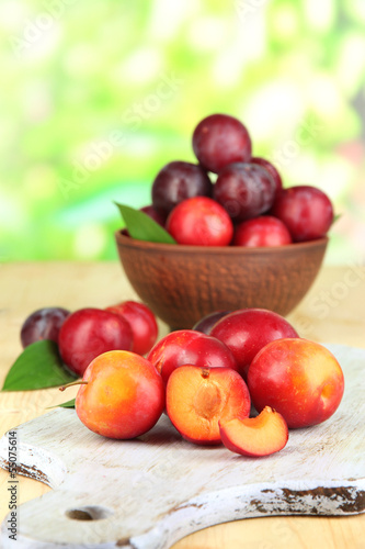 Ripe plums in bowl on wooden table on natural background