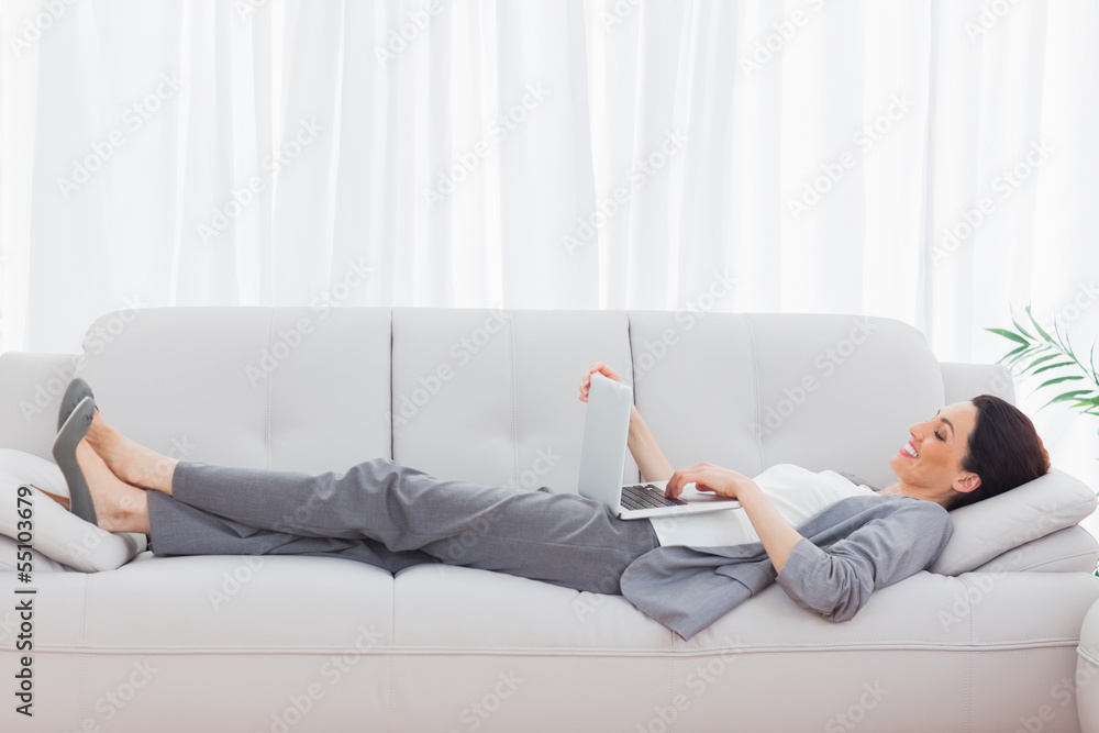 Businesswoman lying on sofa using her laptop Businesswoman lying on sofa using her laptop