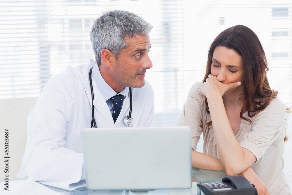 Serious docter showing something on laptop to his patient Serious docter showing something on laptop to his patient