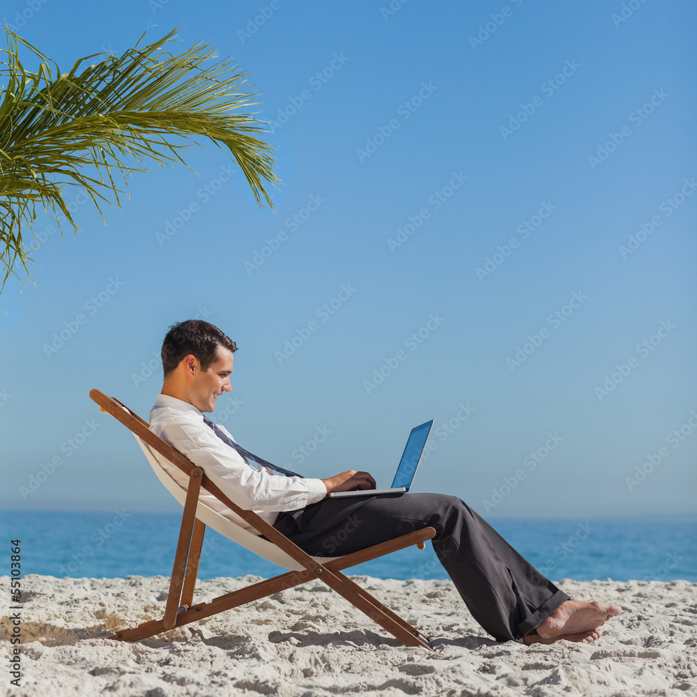 Young businessman on his beach chair using his laptop