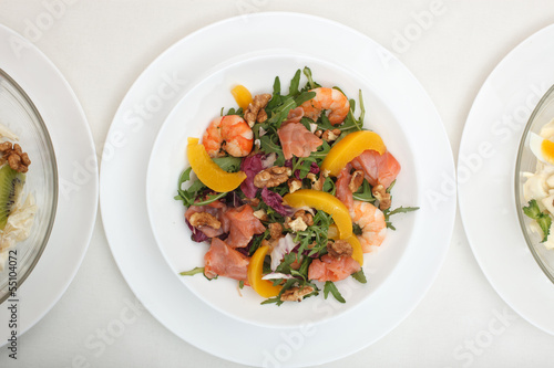 Fresh mixed salad with nuts, shrimps, salmon and peaches close