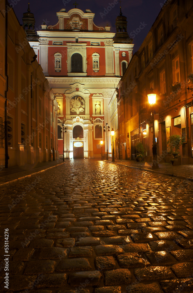 Paved street and parish church in Poznan by night.