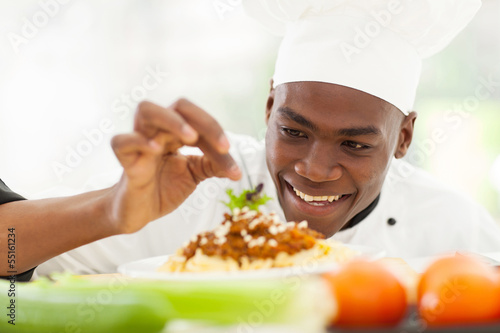 Afro American chef in restaurant kitchen garnishing pasta dish