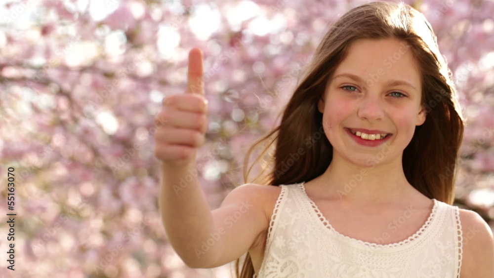 Happy girl giving thumbs up under cherry blossom trees Happy girl giving thumbs up under cherry blossom trees