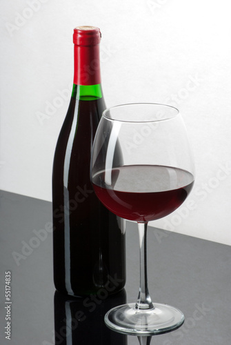Wine bottle and a glass filled with wine on a black reflective s