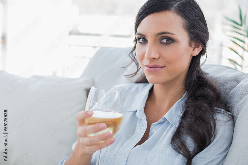 Pretty brunette drinking white wine sitting on sofa Pretty brunette drinking white wine sitting on sofa