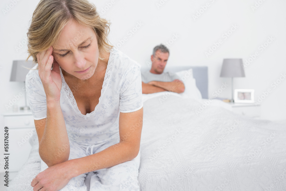 Upset couple sitting on opposite ends of bed after a fight Upset couple sitting on opposite ends of bed after a fight