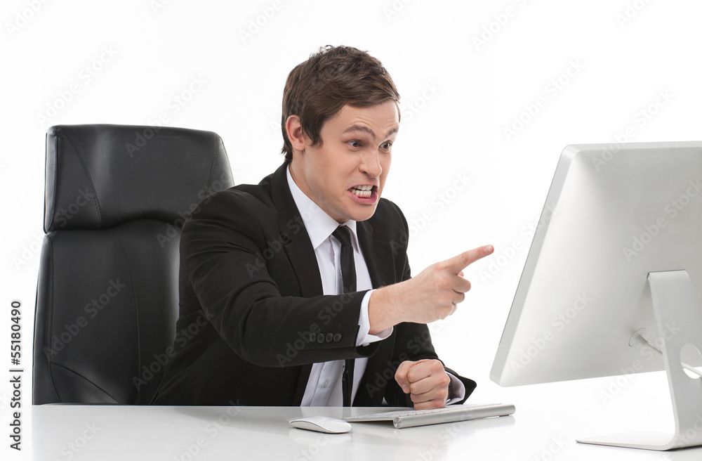 Troubles at work. Furious young businessman pointing computer mo