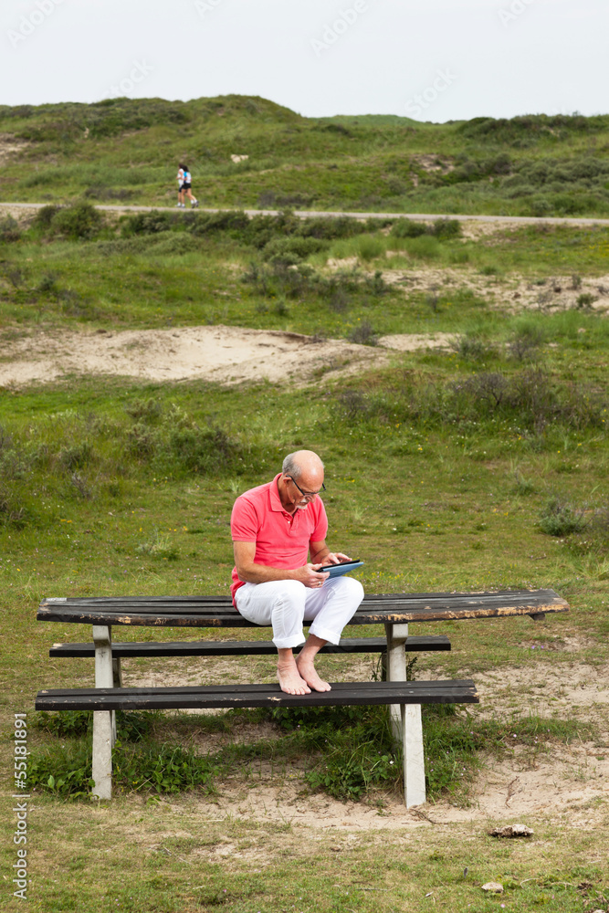 Retired senior man resting and using his tablet at table in park