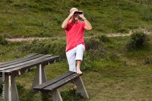 Retired man with beard and glasses using binoculars outdoors in © ysbrandcosijn