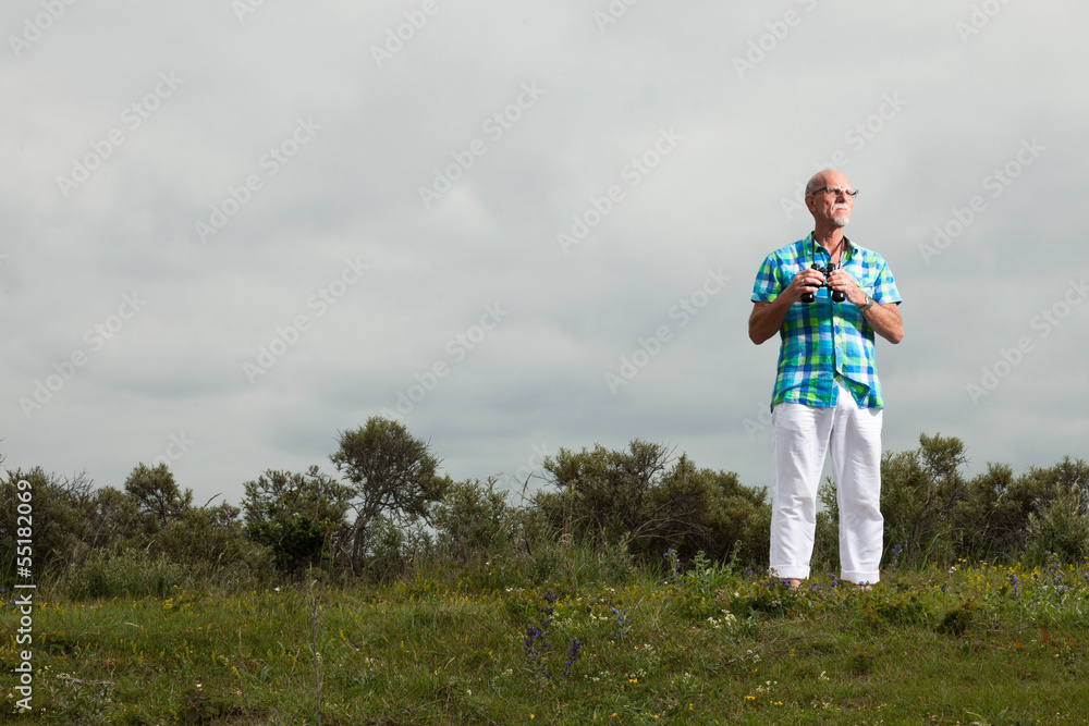 Senior man with beard and glasses using binoculars outdoors in g Senior man with beard and glasses using binoculars outdoors in g
