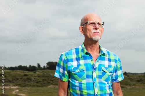 Retired senior man with beard and glasses outdoors in grass dune © ysbrandcosijn