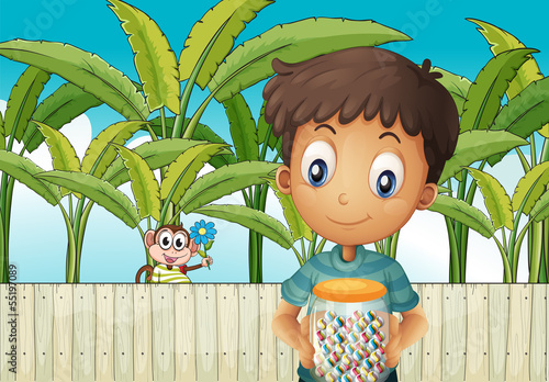A boy with a jar of candies standing in front of the fence with