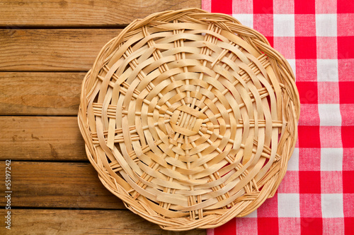 Wicker plate on checked tablecloth over wooden background