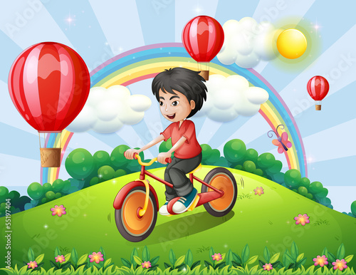 A boy biking at the hilltop with a rainbow and floating balloons