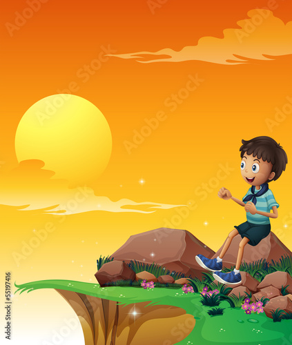 A happy boy sitting at the big rock near the cliff