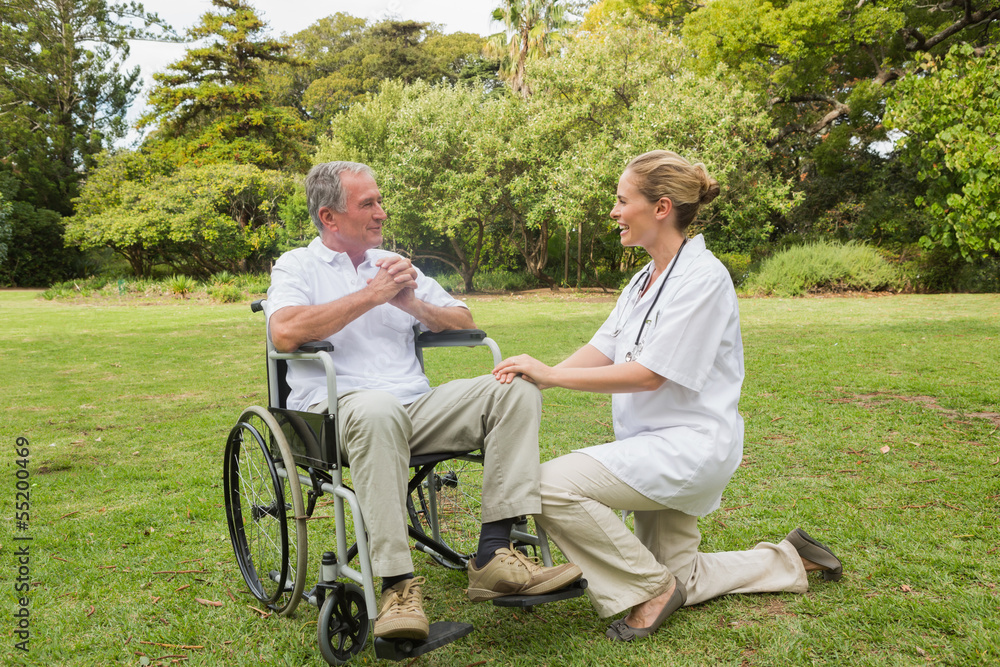 Smiling man in a wheelchair talking with his nurse kneeling besi Smiling man in a wheelchair talking with his nurse kneeling besi