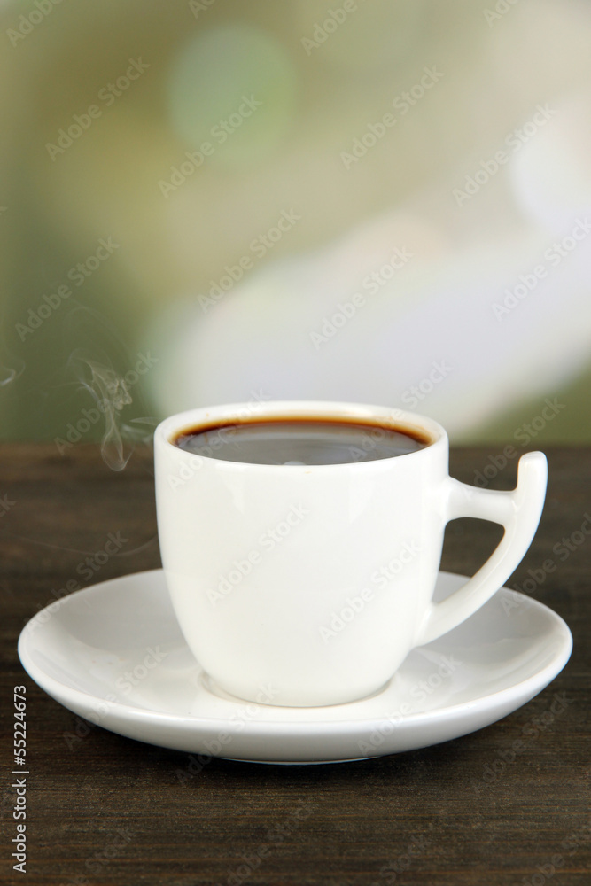 Cup of coffee on wooden table on bright background