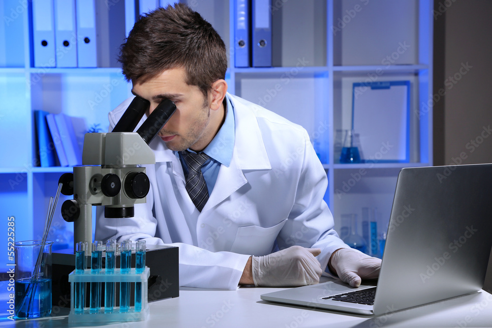 Young laboratory scientist looking at microscope in lab Young laboratory scientist looking at microscope in lab