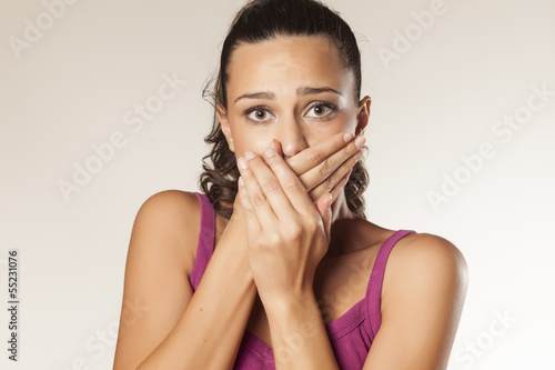 embarrassed young brunette covering her mouth with both hands photo